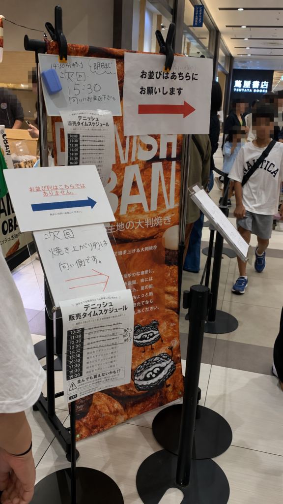 「DANISH OBAN」の焼きたて販売の列を案内するスタンドとタイムスケジュール
